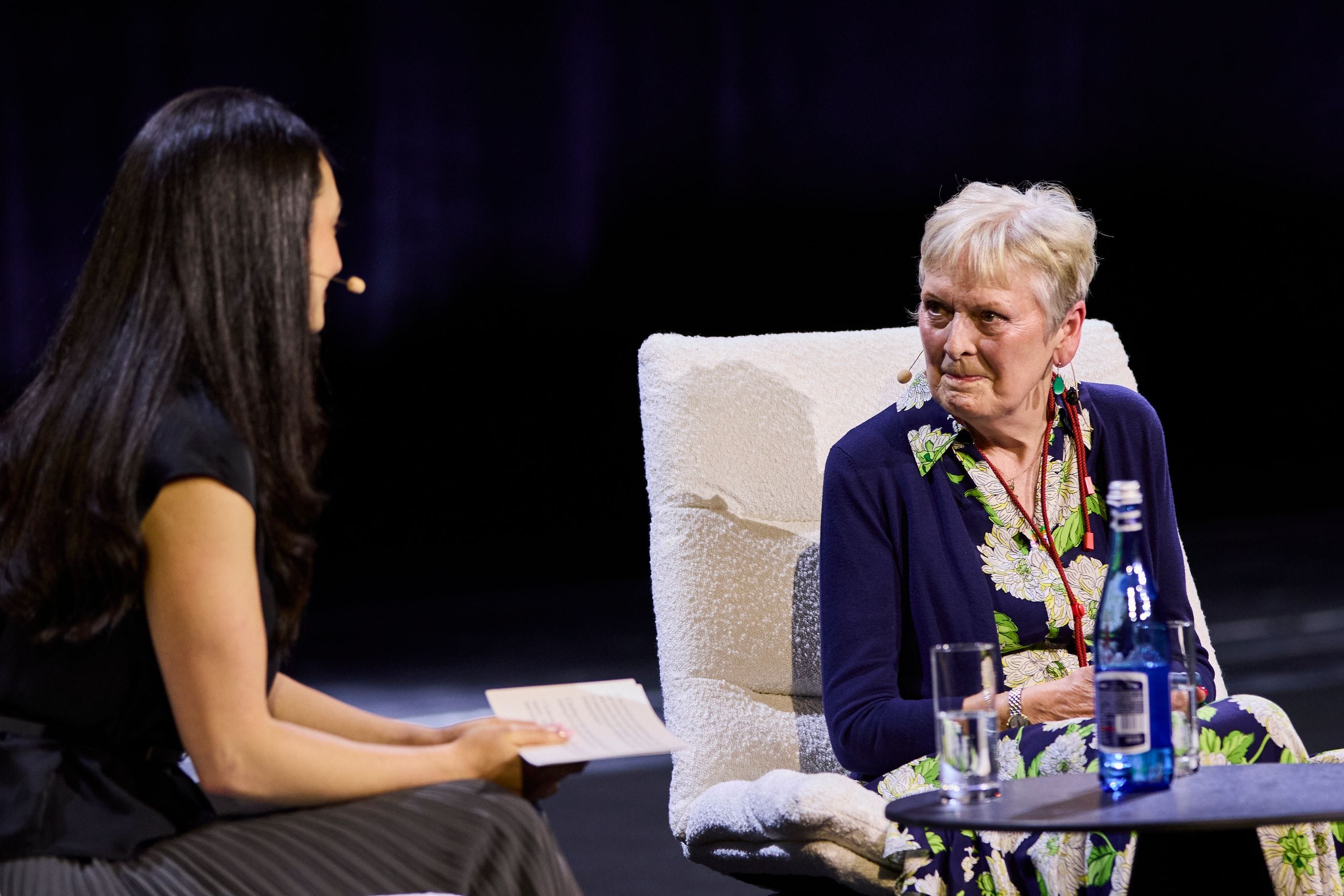 Two people engaged in a conversation on stage, one holding notes.