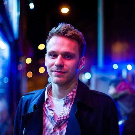 A person standing outdoors at night, surrounded by city lights, wearing a coat and plaid shirt.