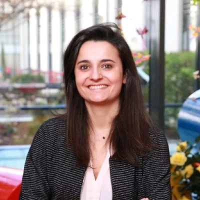 Smiling person in a bright office setting with plants in the background.