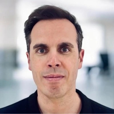 Person with short dark hair, wearing a black shirt, in a bright room.