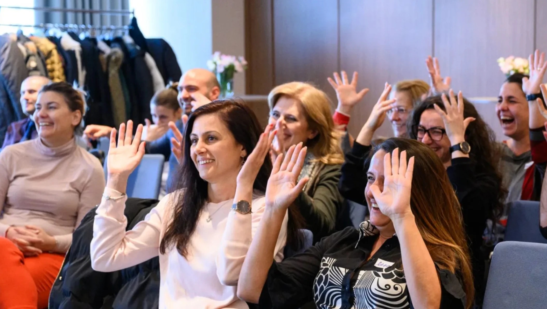 A group of people seated, smiling and doing sign language, engaged in a lively discussion or activity.