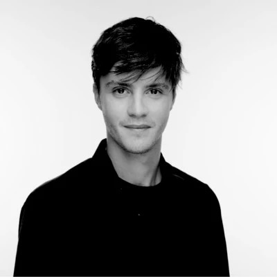 Young man with short dark hair in a black shirt against a plain background.