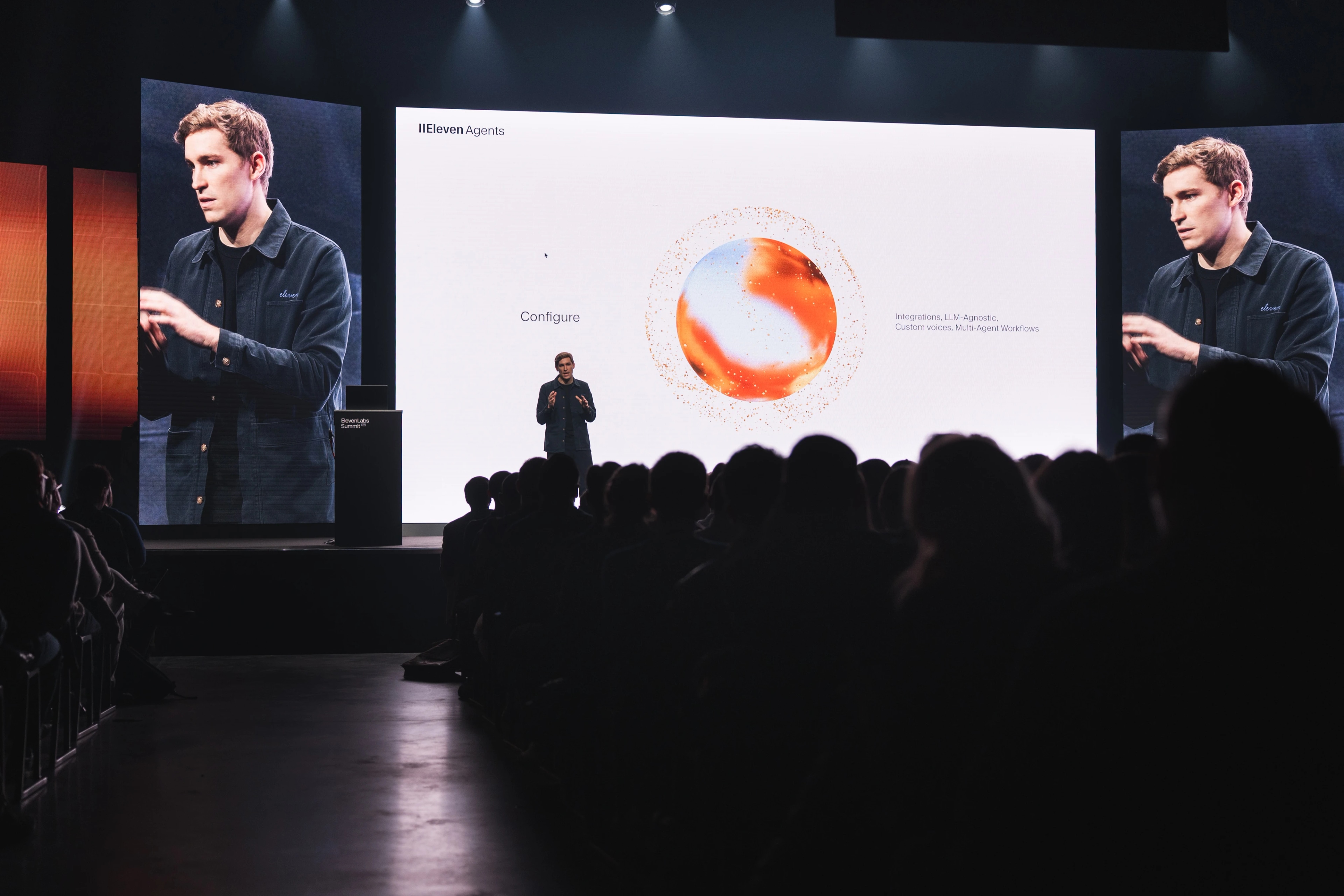 A speaker presents at a tech conference, discussing Eleven Labs' AI integrations on a large screen.