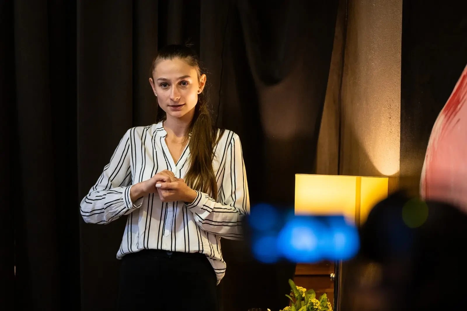 A person in a striped shirt gesturing using sign language while giving a presentation in a softly lit room.