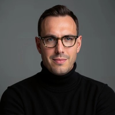 Person wearing glasses and a black turtleneck against a gray background.