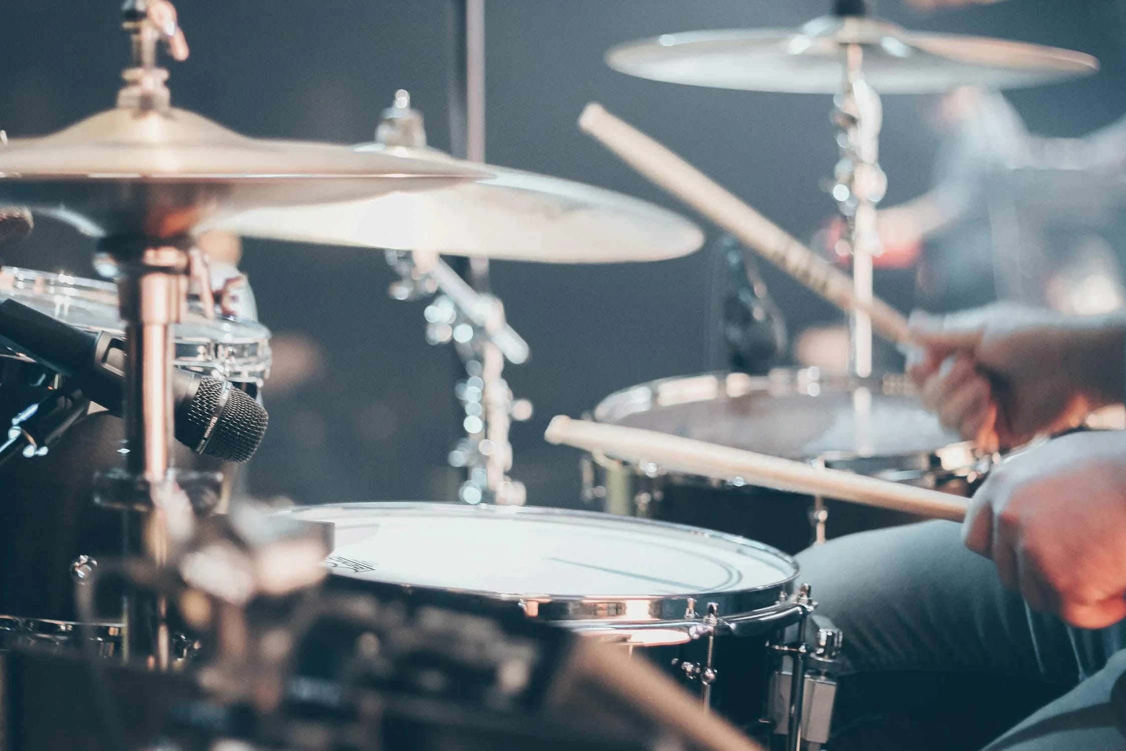 Close-up of a drummer playing a drum kit, with drumsticks in hand and cymbals visible.