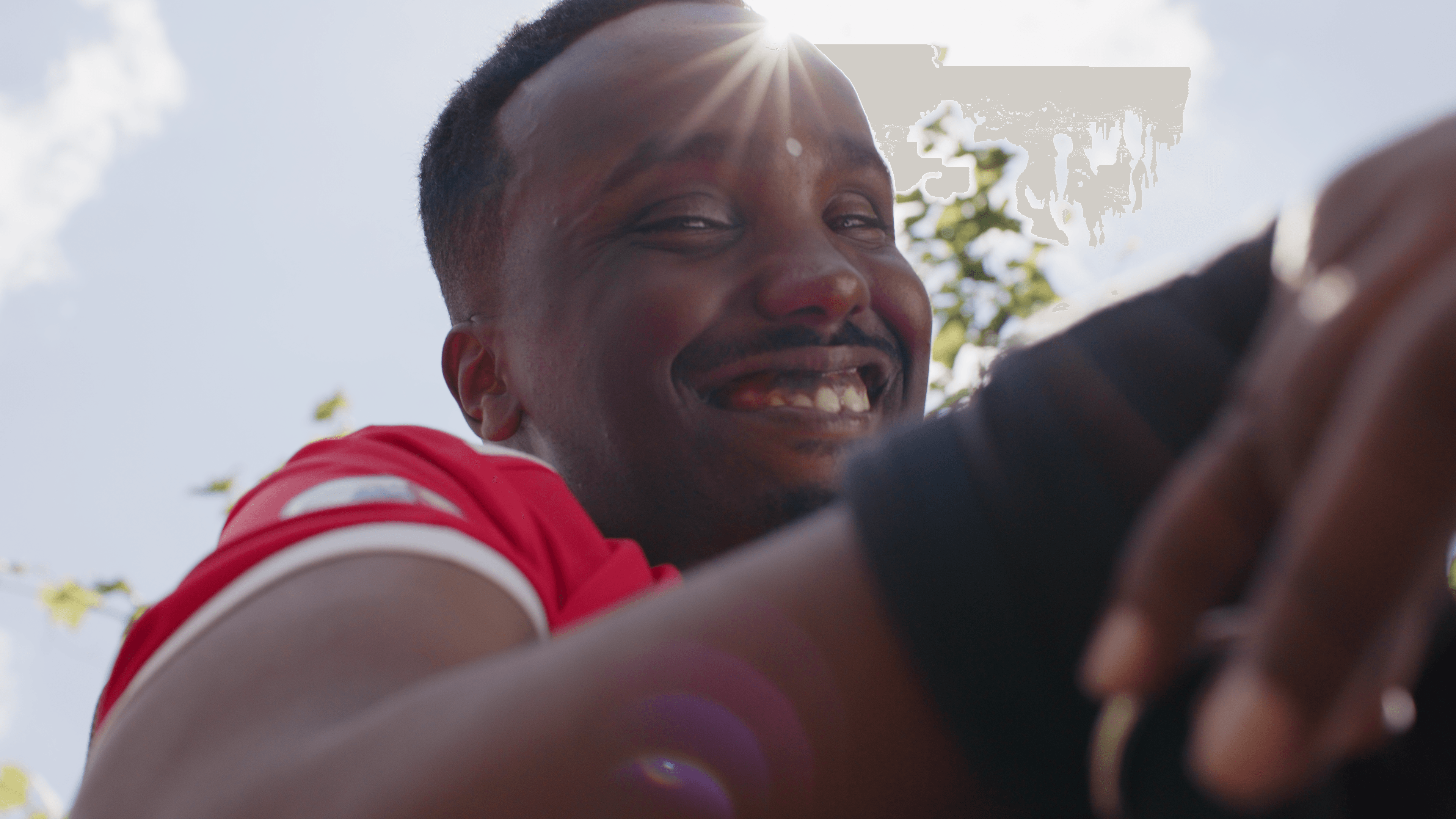 Man looking down and smiling into the camera, the sun shines behind him