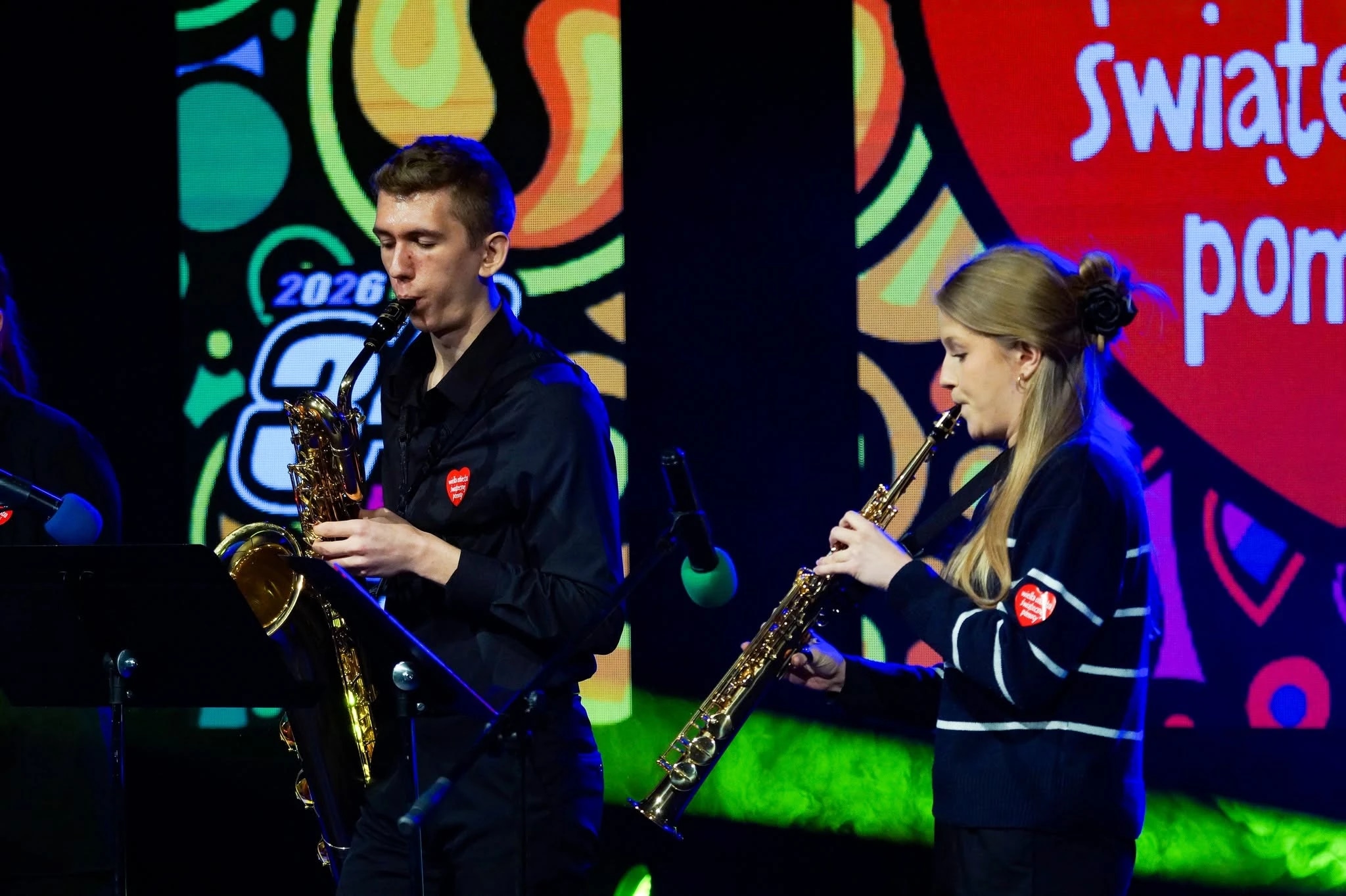 Two musicians playing saxophones on stage with colorful background.
