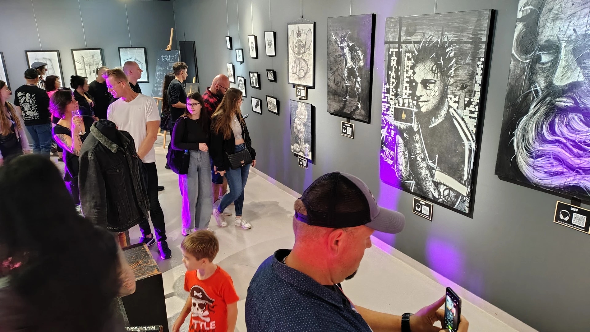People viewing art in a gallery with vibrant lighting and various paintings on display.