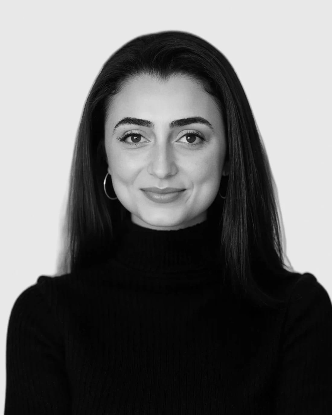 Portrait of a smiling woman with long dark hair wearing a black turtleneck.