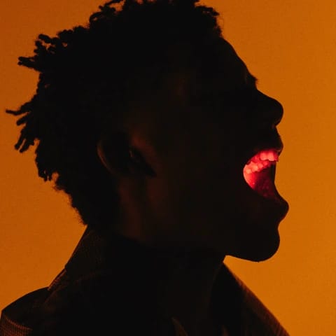 Person in silhouette yelling with glowing light in their mouth, set against an orange background.