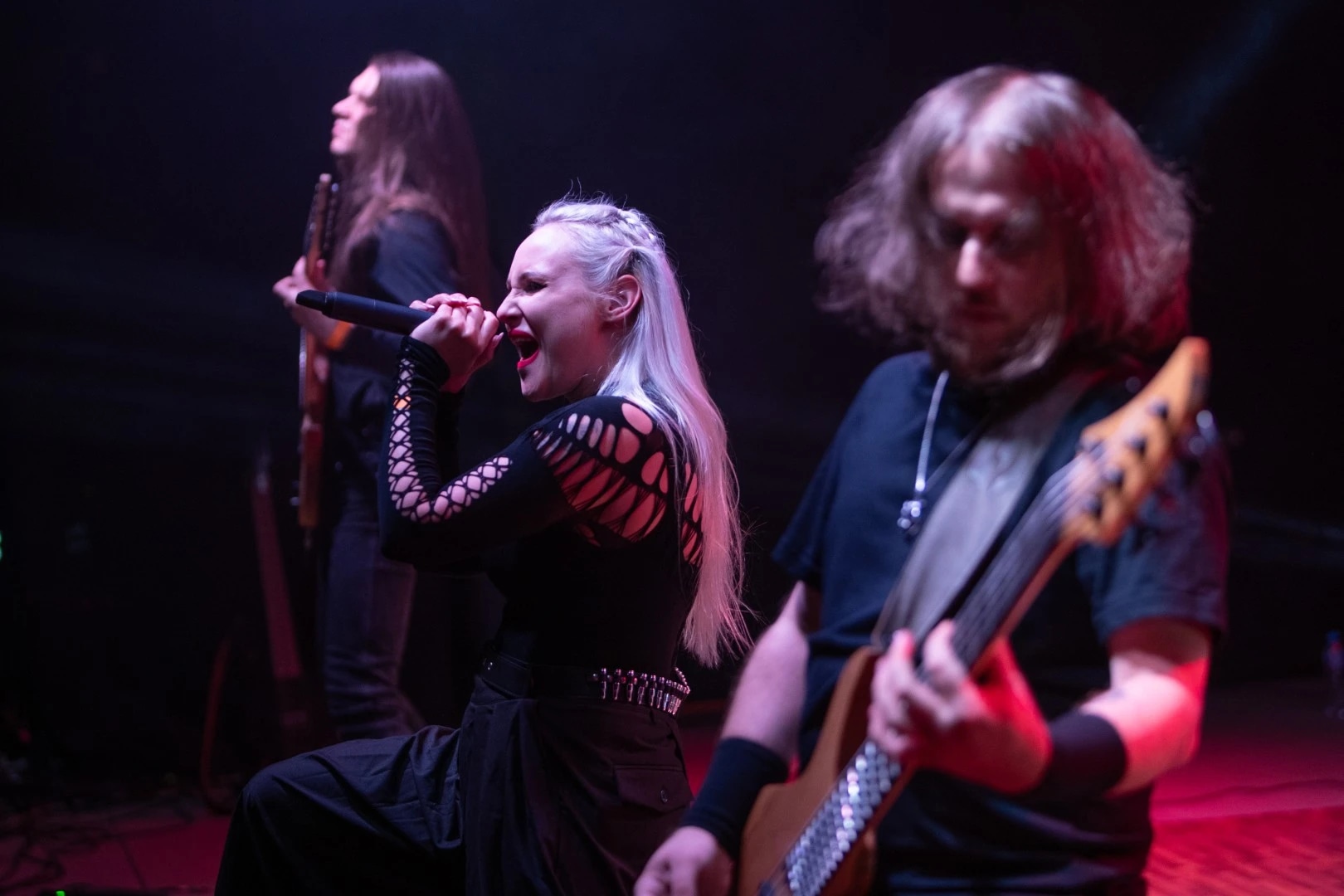 Three musicians on stage: a vocalist passionately singing, flanked by two guitarists.